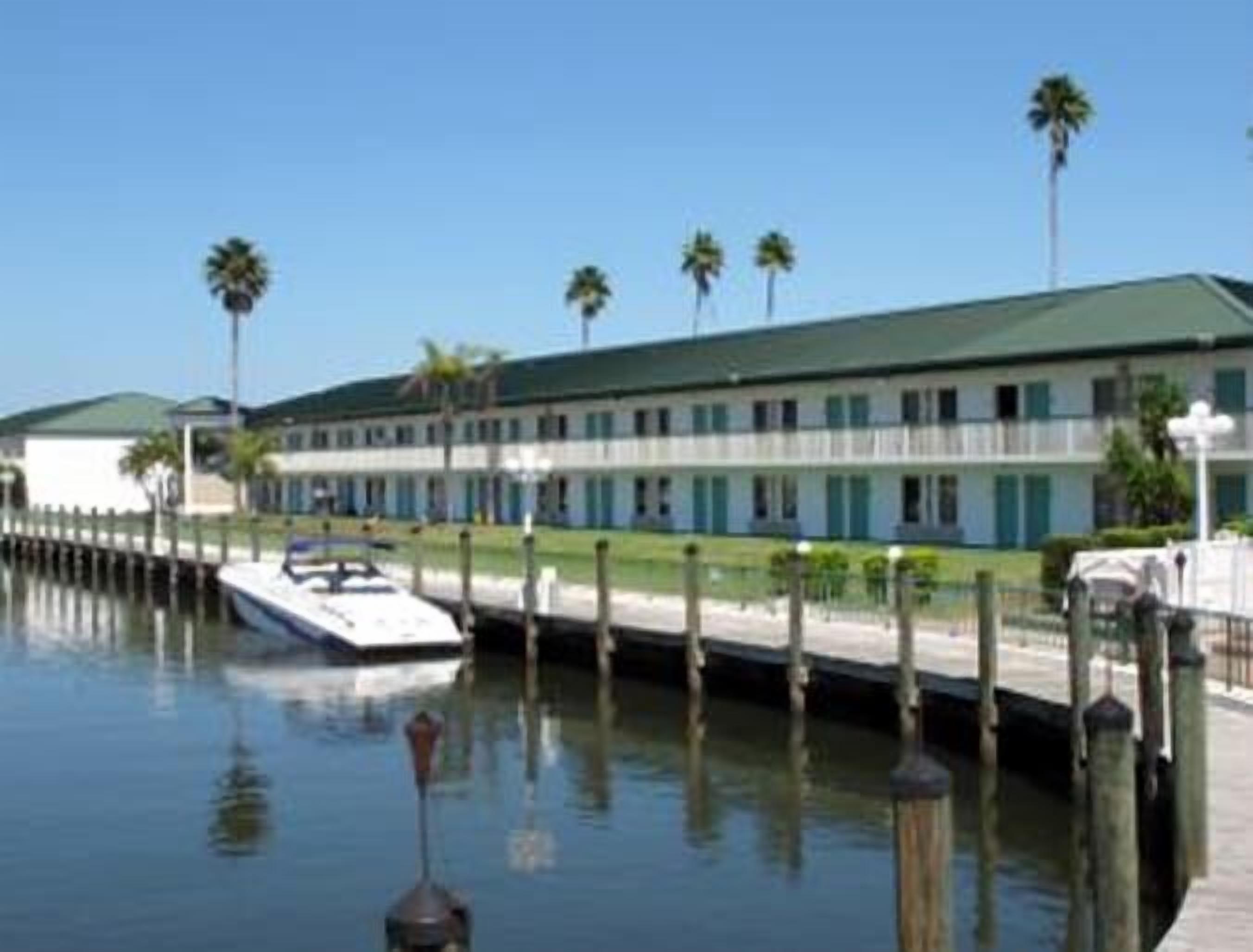 Un hotel frente al mar con un muelle, un barco y una hilera de palmeras.