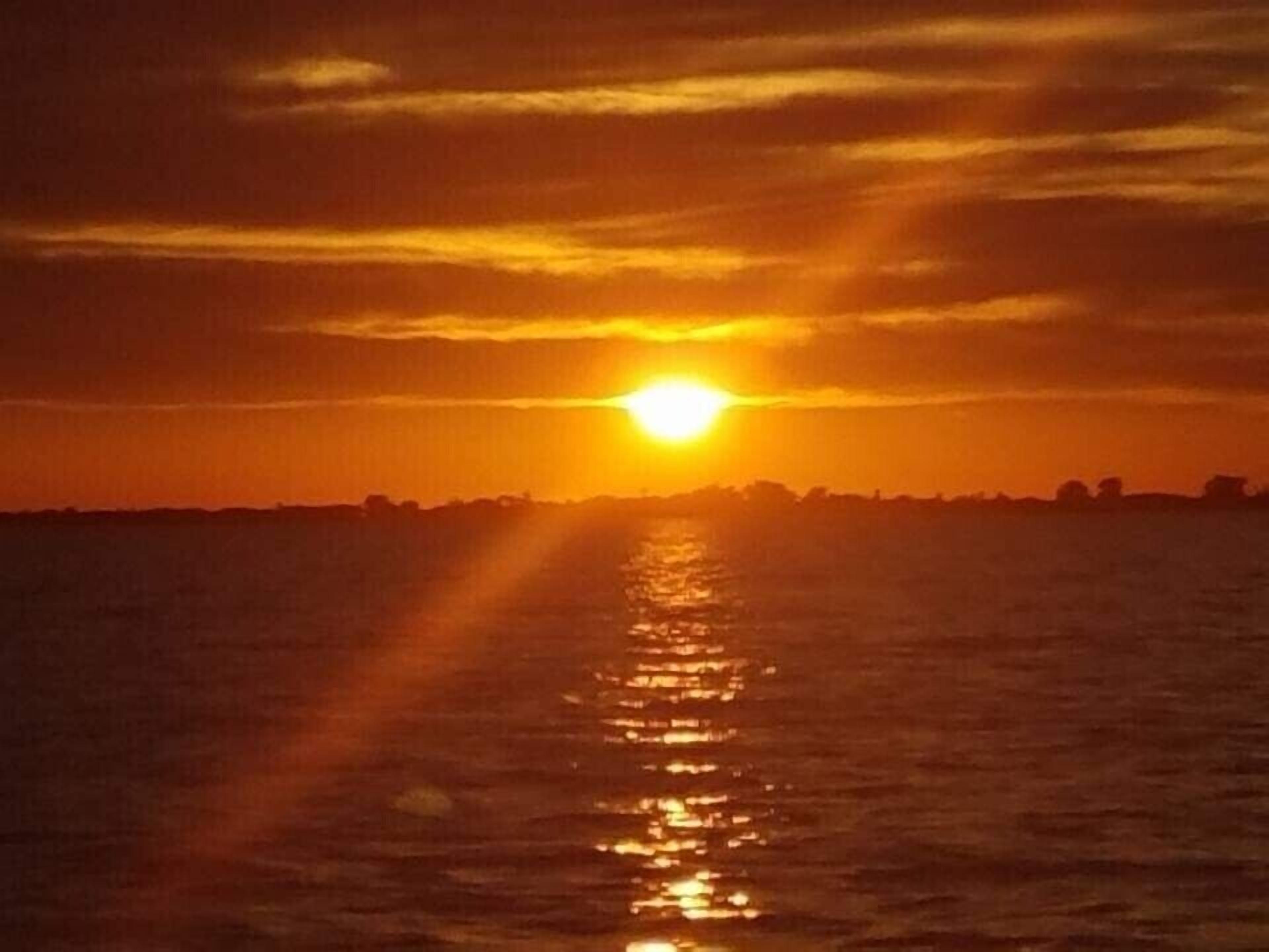 A sunset over a body of water with a silhouette of a distant city skyline.