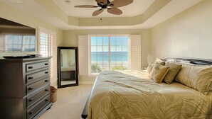 Ein Schlafzimmer mit Bett, Kommode, Deckenventilator, Fenster mit Meerblick und einer Schiebetür.