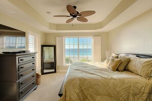Ein Schlafzimmer mit Bett, Kommode, Deckenventilator, Fenster mit Meerblick und einer Schiebetür.