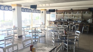 A restaurant with multiple tables and chairs, a bar area with various bottles, and a television mounted on the wall.