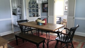Een eetgedeelte met een houten tafel, vier stoelen, een bank, een kroonluchter en een keuken op de achtergrond.
