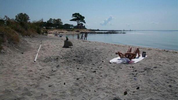 Een strand met een zandstrand, een persoon die op een handdoek ligt, en nog een paar anderen op de achtergrond.