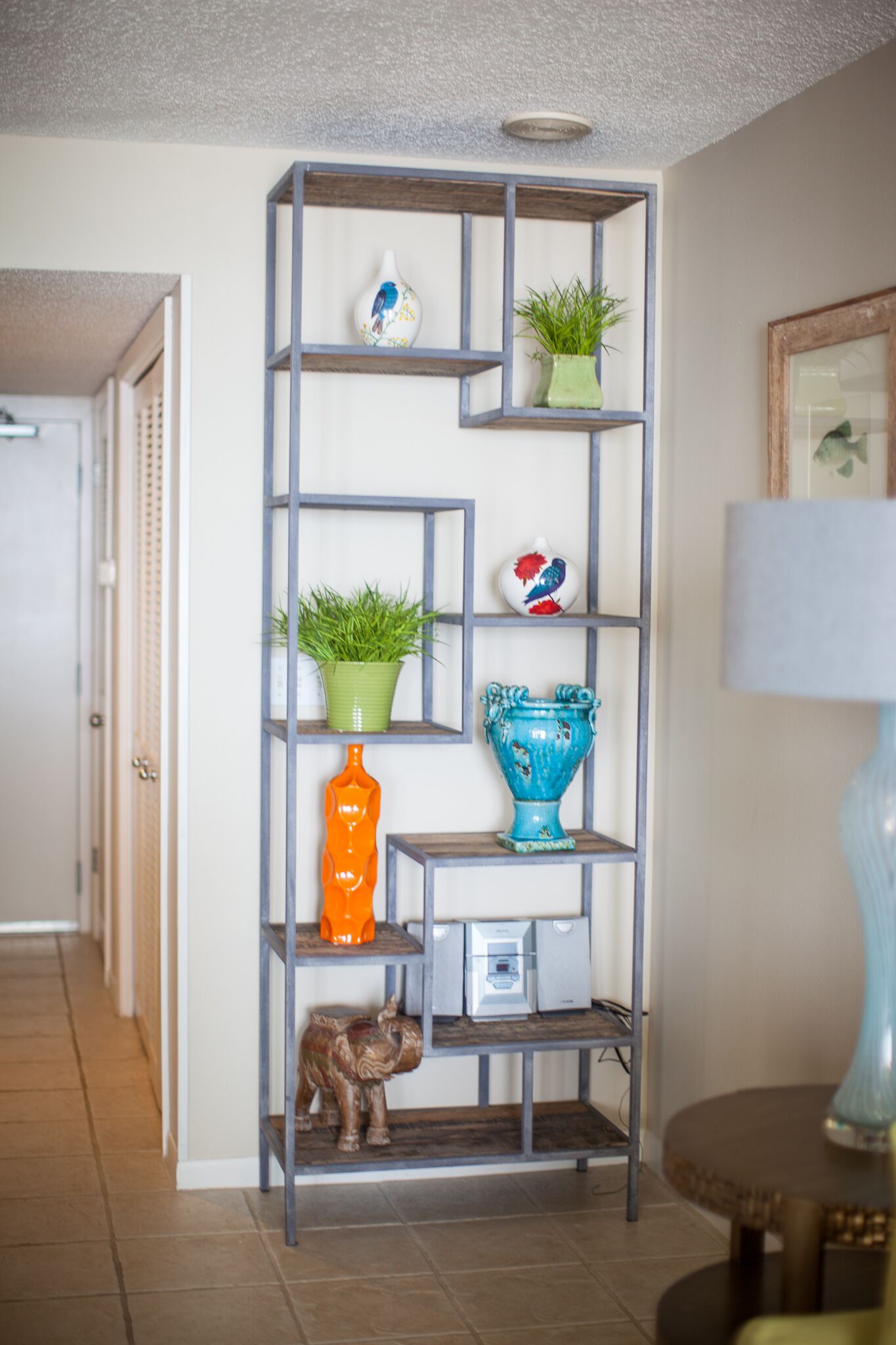 A hallway with a grey metal shelving unit displaying various decorative items.