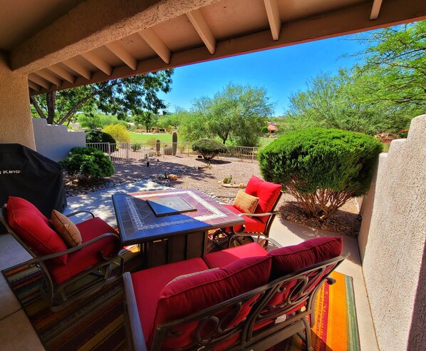 An outdoor patio with a table and chairs, a covered seating area, and a view of a landscaped garden.
