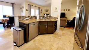 A modern kitchen with a dishwasher, a sink, and a refrigerator. There is a dining area with a table and chairs.