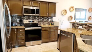 A modern kitchen with stainless steel appliances, a tiled backsplash, and wooden cabinets.