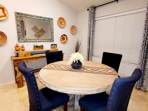 A dining area with a round table, blue upholstered chairs, a mirror, and decorative plates on the wall.