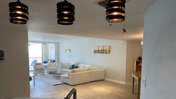 A modern living room with a white sofa, a coffee table, and a dining area with a marble countertop and a sink. - SPACIOUS OCEAN FRONT PARADISE (Fort Pierce)