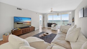 Una sala de estar moderna con un televisor de pantalla plana grande, un sofá, una mesa de centro y vistas al océano a través de amplios ventanales.