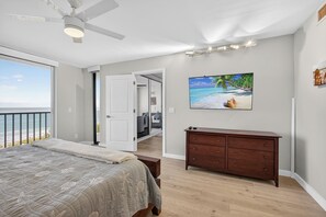 Un dormitorio con una cama grande, un aparador, un ventilador de techo y un cuadro de una playa.