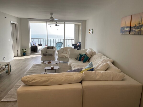 Un salon spacieux avec un grand canapé blanc, une table basse et un balcon offrant une vue sur la mer.