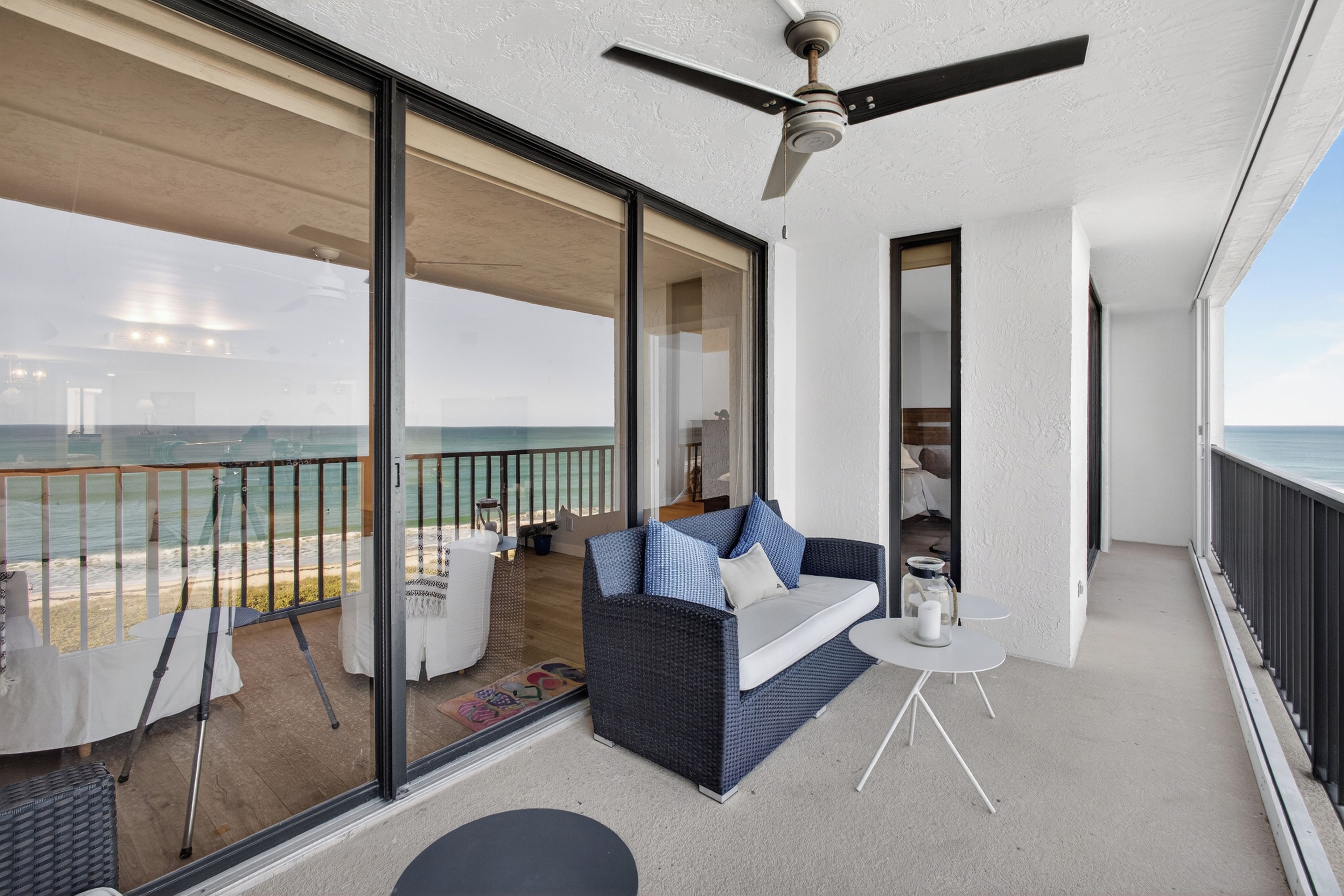 A balcony with a view of the ocean, a sofa, a small table, and a ceiling fan.