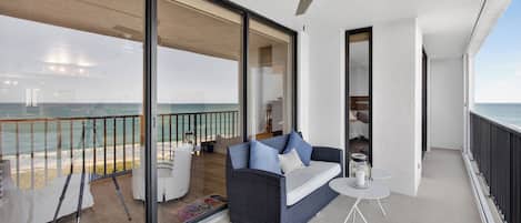 A balcony with a view of the ocean, a sofa, a small table, and a ceiling fan.