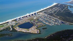 Vista aérea de una zona costera con un puerto deportivo, una gran extensión de agua y una playa.
