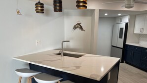 A modern kitchen with a large island, bar stools, pendant lighting, and a fish decoration on the wall. - SPACIOUS OCEAN FRONT PARADISE (Fort Pierce)