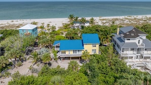 A beachfront property with multiple houses, including a large house with a blue roof and a smaller house with a blue roof, surrounded by lush greenery and a sandy beach.