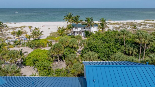 A beachfront property with a white house, palm trees, and a view of the ocean.