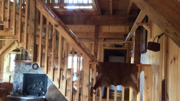 Interior de madera con chimenea de piedra, un sofá y una vaca colgante.