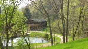 A cabin with a wooden deck overlooking a lake, surrounded by lush greenery and trees.
