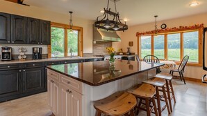 A kitchen with a large island, dark cabinets, and a view of the outdoors.