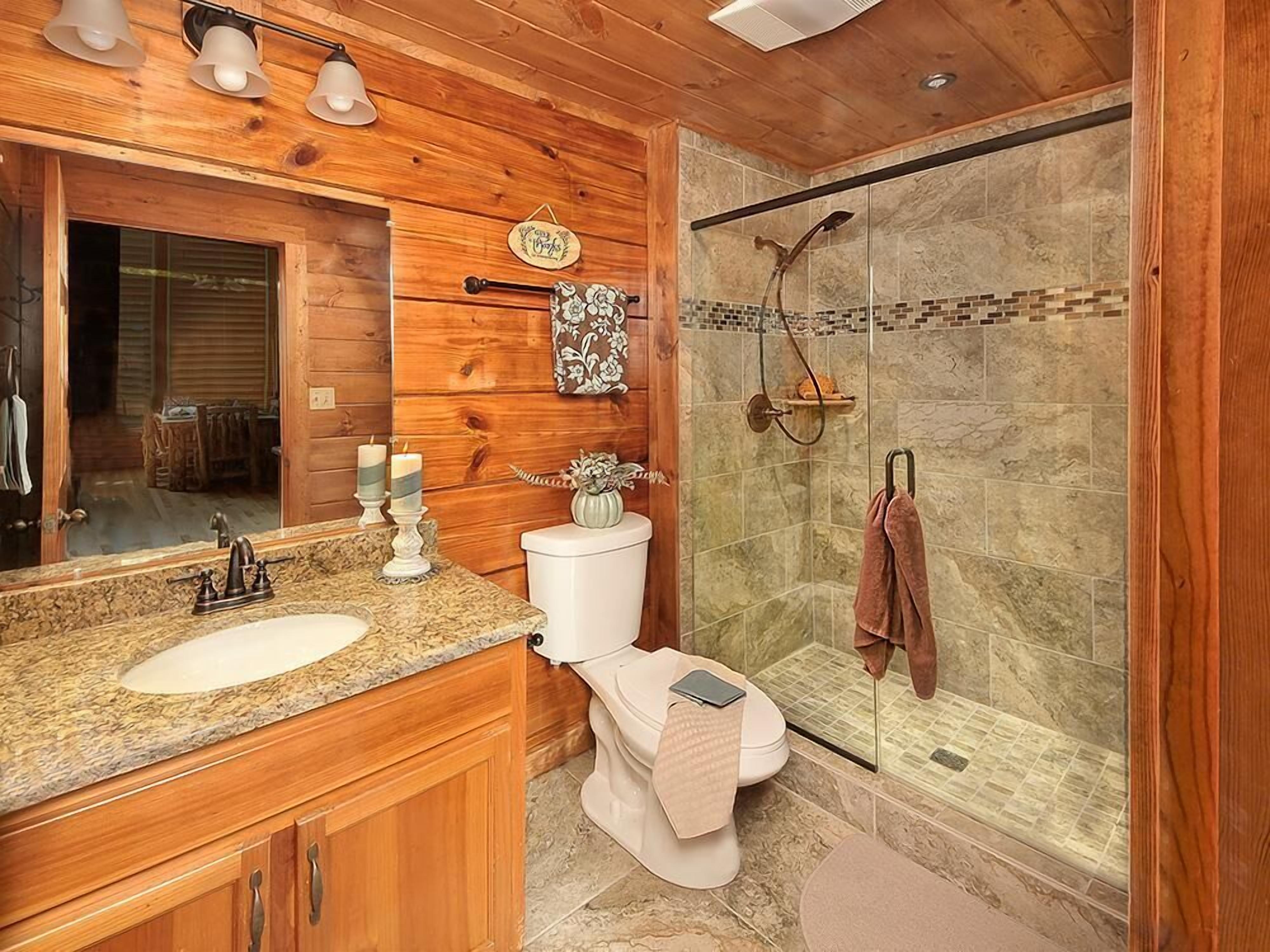 A bathroom with wooden paneling, a granite countertop, a toilet with a towel, and a glass shower enclosure.