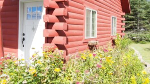 Una casa de madera roja con puerta blanca y dos ventanas.