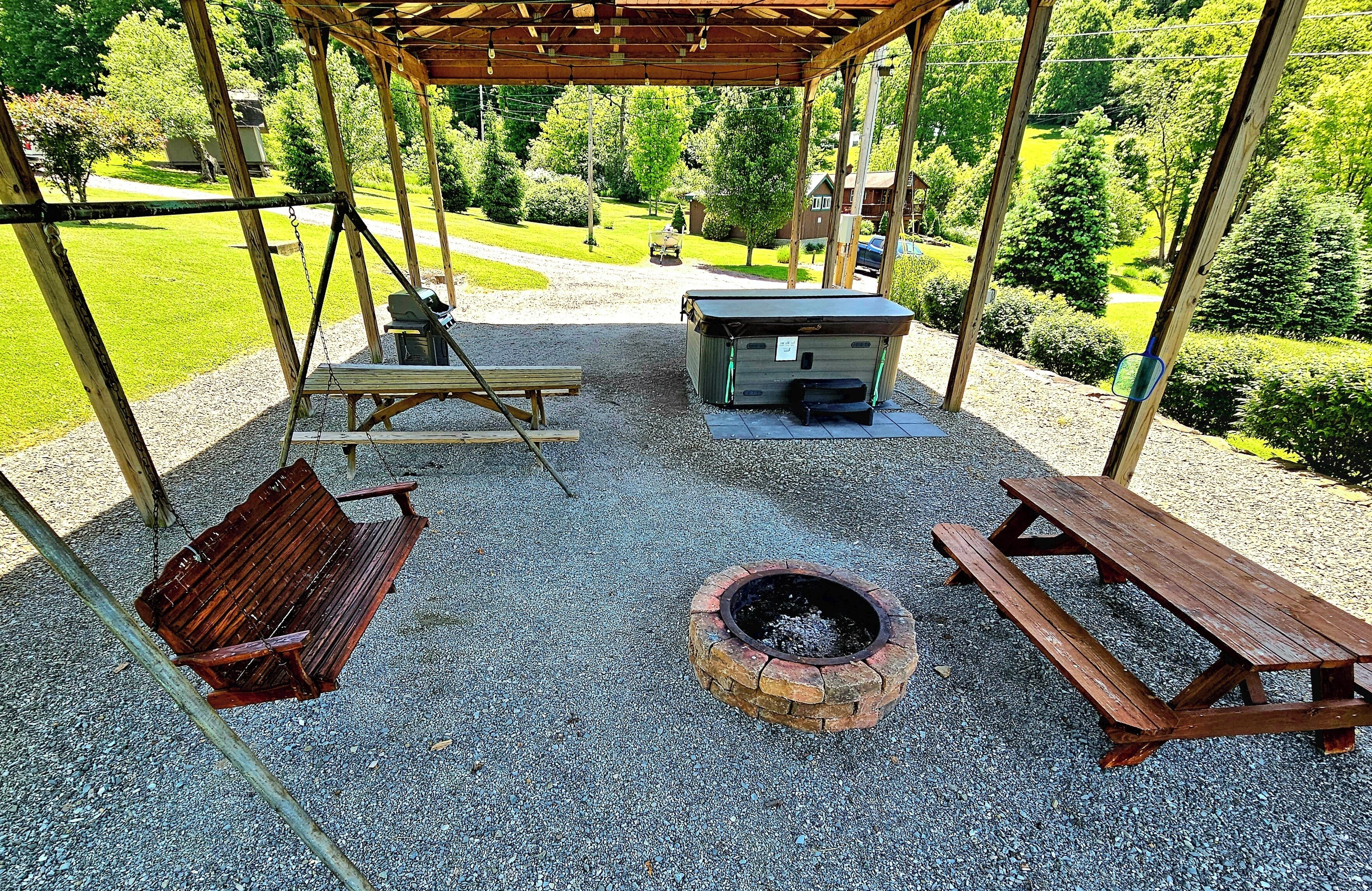 Un espace extérieur aménagé, abrité, avec des balançoires, un foyer et des tables de pique-nique.