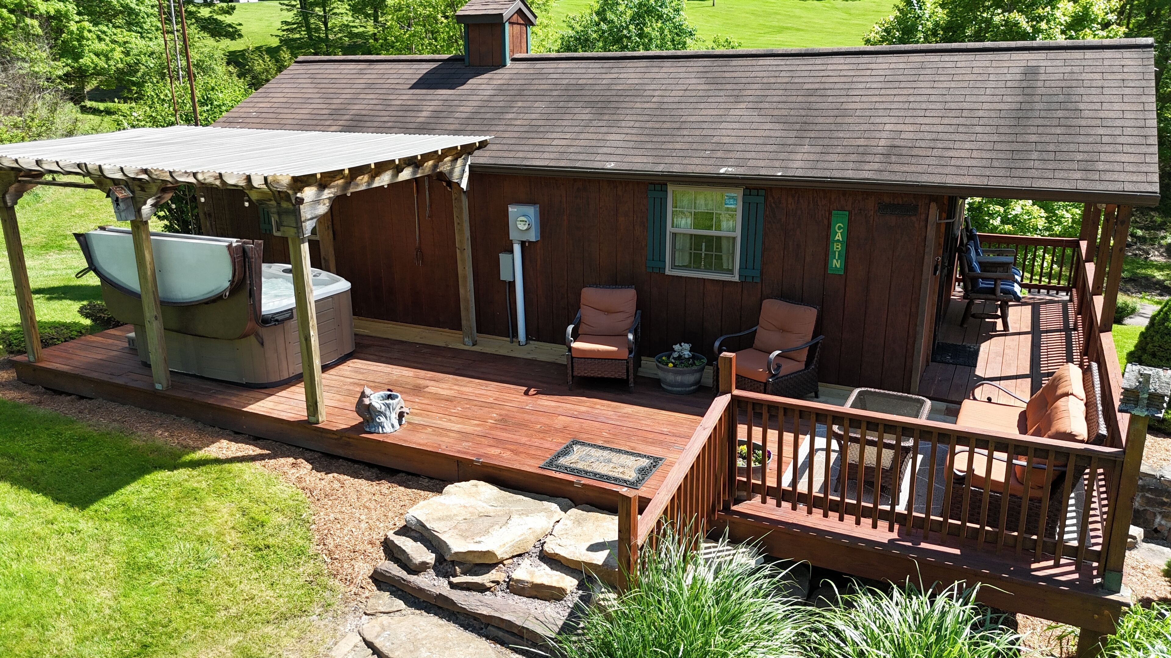 Een houten hut met een hottub, twee comfortabele stoelen, een stenen openhaard en een terras met een reling.