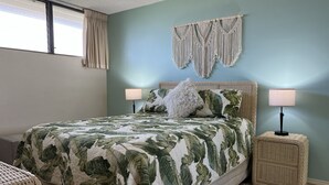 A bedroom with a bed, two bedside lamps, a macrame wall hanging, and a window with curtains. - Cozy Top-Floor  Maui Parkshore Condo (Kihei)