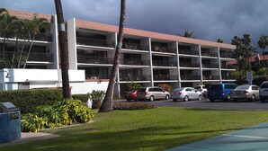 A multi-story hotel with balconies, a parking lot, and palm trees. - Cozy Top-Floor  Maui Parkshore Condo (Kihei)