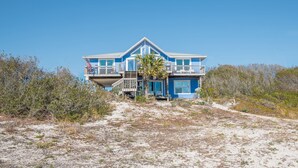 Ein zweistöckiges Strandhaus mit Balkon, einer Flagge und einer Palme.