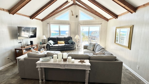 Ein geräumiges Wohnzimmer mit einer großen Eckcouch, einem weißen Couchtisch mit Kerzen und einem Fernseher.