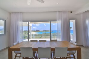 Enjoy a meal at the large dining table surrounded by four chairs, with a stunning ocean view through the floor-to-ceiling windows.