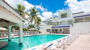 A pool area with lounge chairs, palm trees, and a building with multiple balconies. - Stunning Penthouse on Mullet Bay beach (Cupecoy)