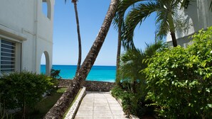 A pathway leading to a beach with palm trees and a white building with arched windows. - Stunning Penthouse on Mullet Bay beach (Cupecoy)