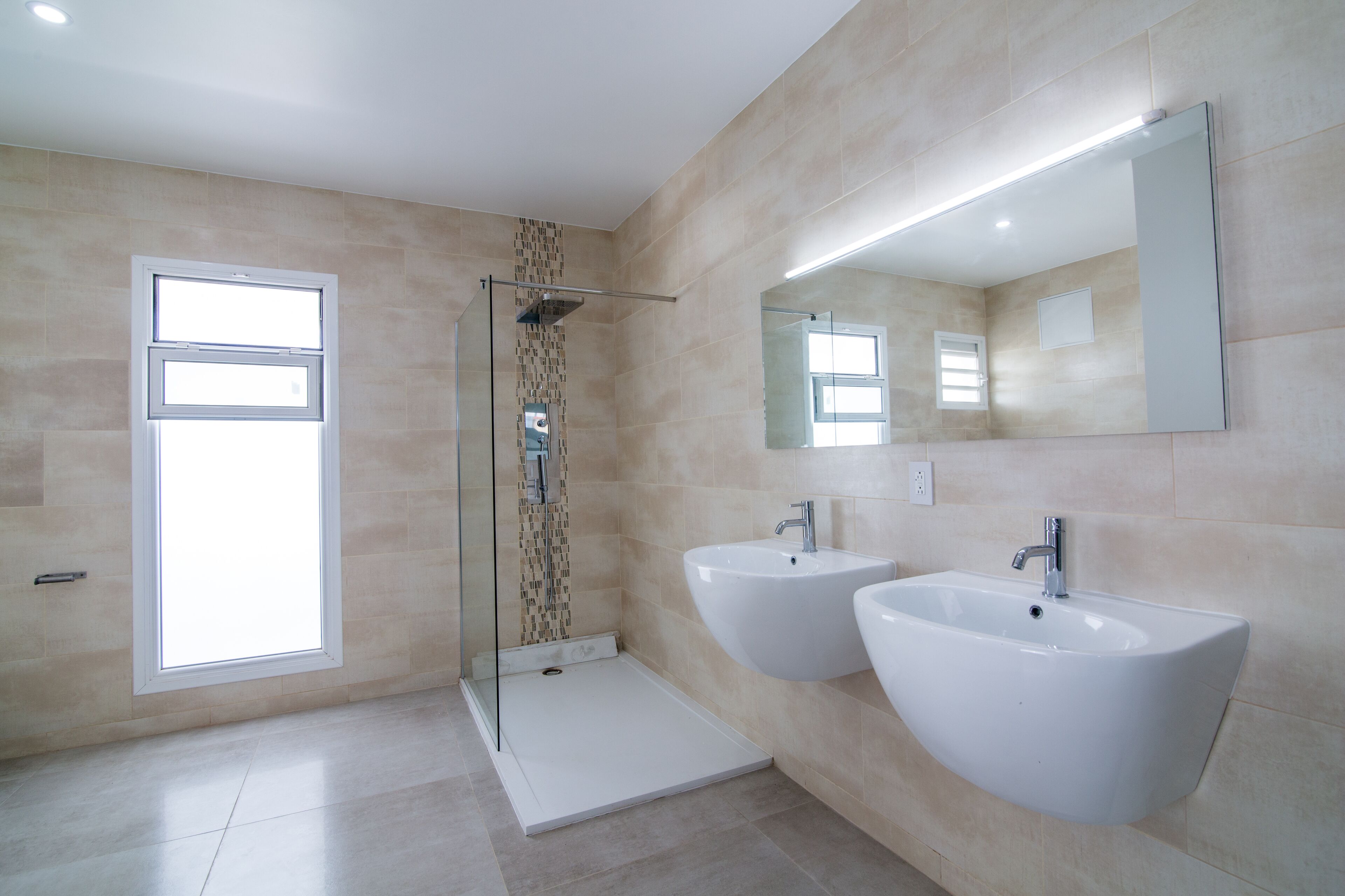 Un baño moderno con dos lavabos, cabina de ducha con mampara de vidrio y un espejo grande.