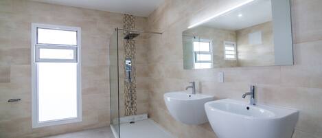 Un baño moderno con dos lavabos, cabina de ducha con mampara de vidrio y un espejo grande.