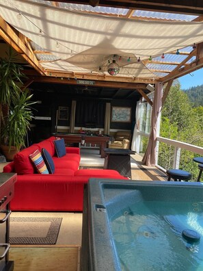 A cozy outdoor seating area with a red sofa, a hot tub, and a wooden pergola. -  RIVERFRONT, KAYAKS, DOCK, YARD, VIEW,  HOT TUB, POOL TABLE, BBQ, 5 STAR  (Guerneville)