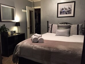 A neatly made bed with rolled towels, a bedside table with a lamp, a framed picture on the wall, and a door leading to another room. -  RIVERFRONT, KAYAKS, DOCK, YARD, VIEW,  HOT TUB, POOL TABLE, BBQ, 5 STAR  (Guerneville)