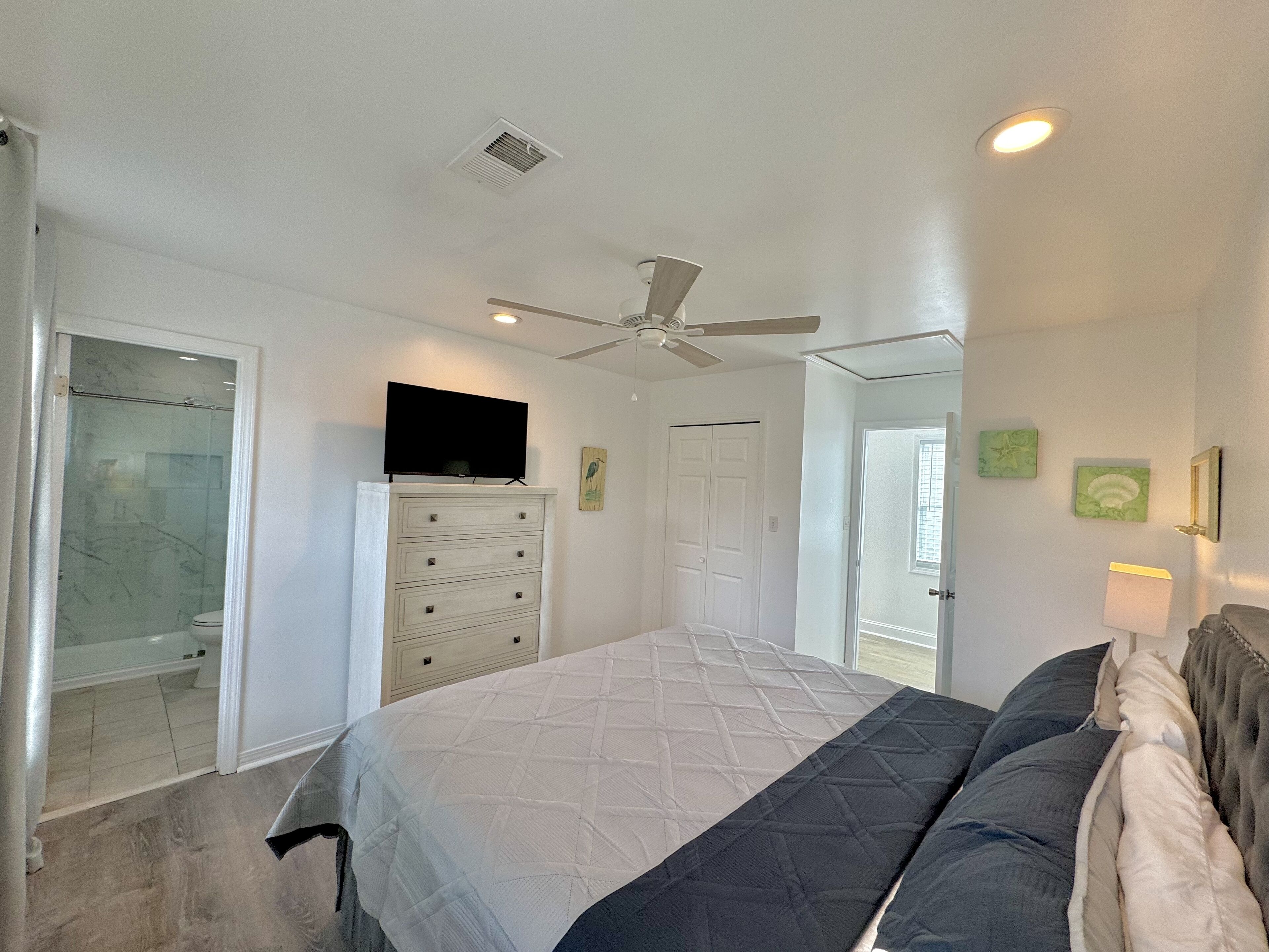 Une chambre à coucher comprenant un lit, un ventilateur de plafond, une télévision, une commode et un dressing.