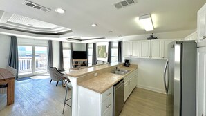 A modern kitchen with white cabinets, a stainless steel refrigerator, and a large island with a sink. - New Renovation 2024 Direct Gulf View! White Beach Dolphins 4 Bedrooms, 3.5 bath (Gulf Shores)