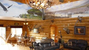A log cabin interior with a dining area, two sofas, a chandelier, and wall-mounted animal heads. - Luxurious & Spacious!  A Great Place For Family, Friends, Reunions & Corporate! (Adams)
