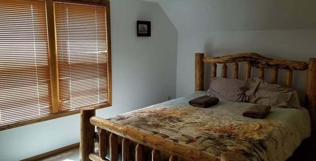 A bedroom with a wooden headboard, a bed with a floral bedspread, and a window with blinds.