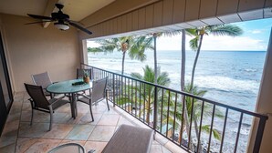 Un balcón con mesa y sillas, con vista a una playa con palmeras y el océano.