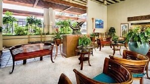 Un vestíbulo espacioso con mobiliario de madera, plantas en macetas y vistas al exterior con vegetación.