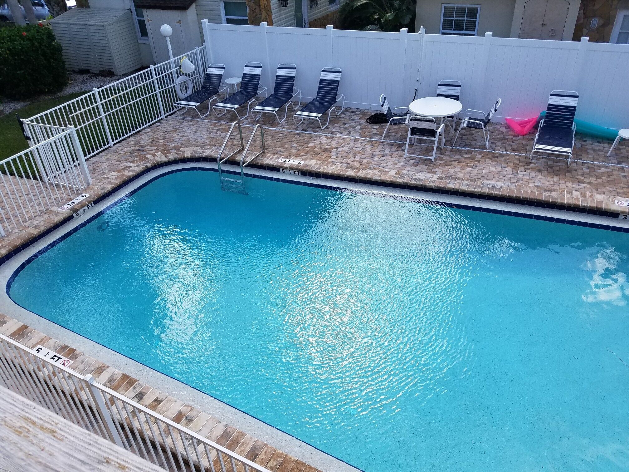A rectangular pool with a white deck, lounge chairs, and a small table.