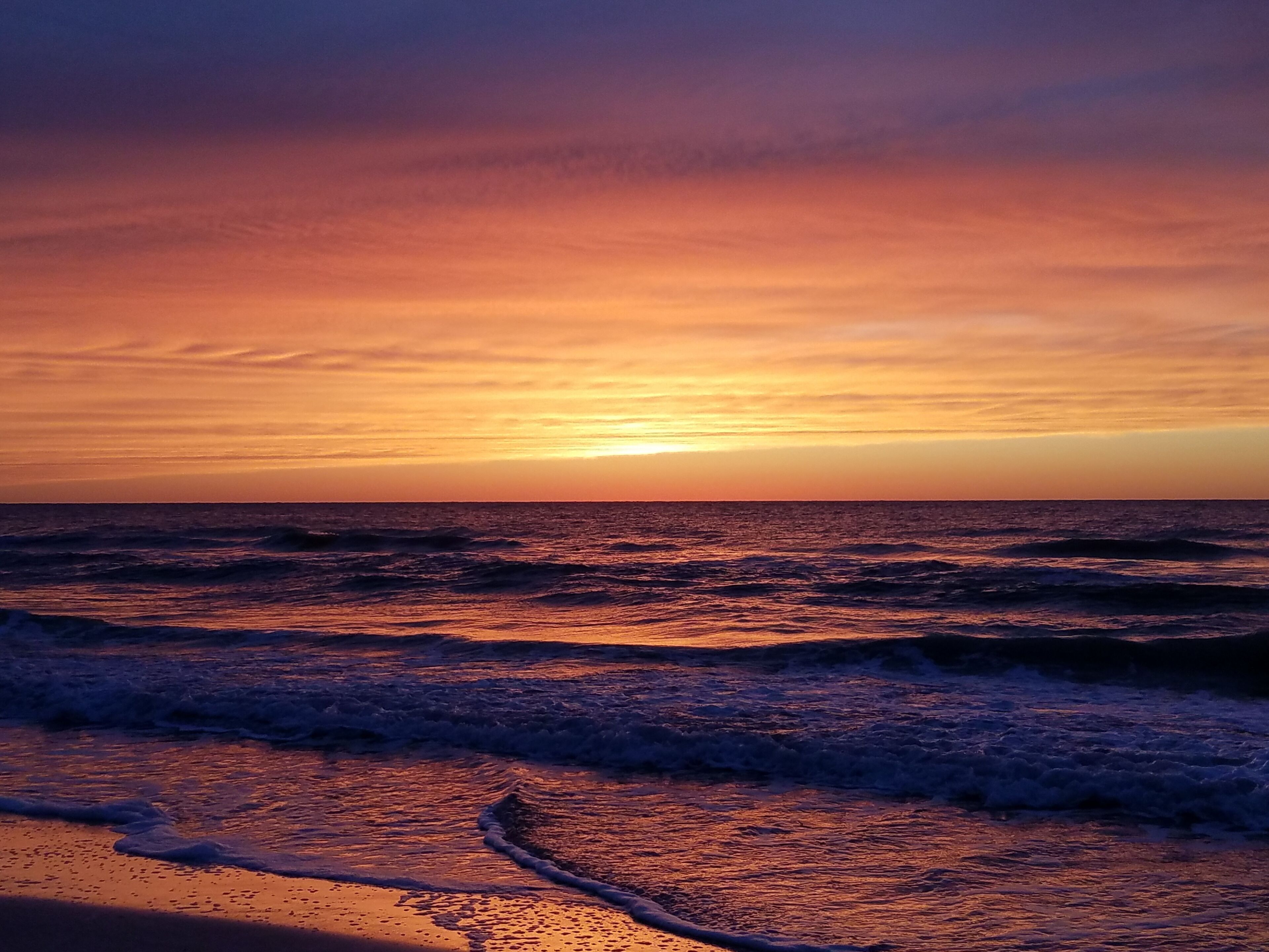 A sunset over the ocean with waves approaching the shore.