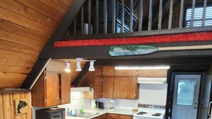 Een keuken met houten kasten, een wit kookeiland met stoelen, en een trap die naar een hoger niveau leidt.