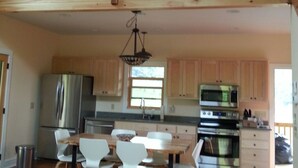 A spacious loft-style kitchen with high ceilings, wooden beams, and a dining area with white chairs and a wooden table.